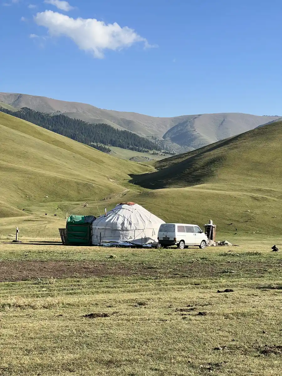 Yurt camp with a van parked beside it in the green rolling hills of the Assy Plateau